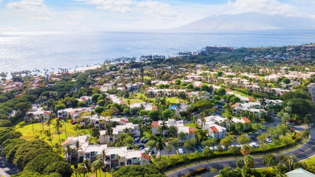 Aerial view of The Palms at Wailea condos surrounded by tropical landscaping with views of the Pacific Ocean and West Maui Mountains