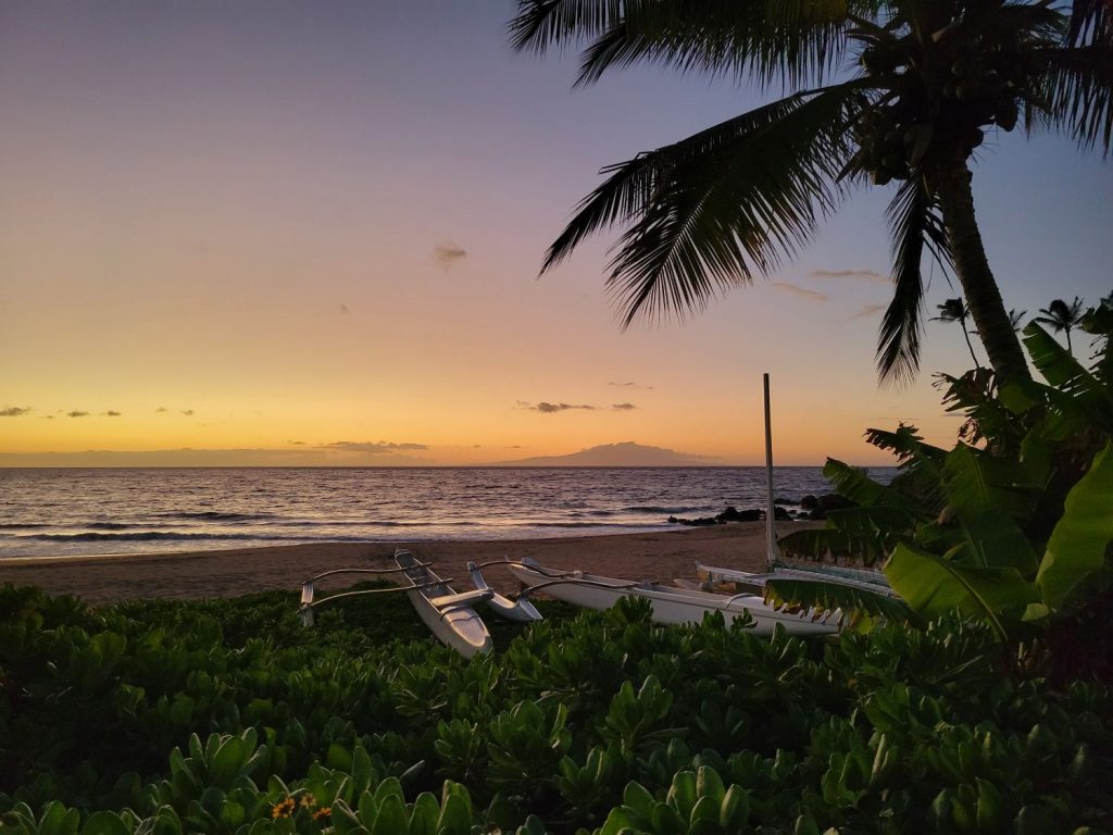 Sunset over Polo Beach in Wailea, Maui with outrigger canoes and palm trees in the foreground