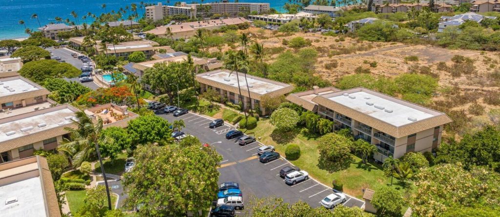 Aerial view of Kihei Kai Nani condo complex in South Kihei, Maui, with swimming pool, low-rise buildings, tropical landscaping, and ocean in the background