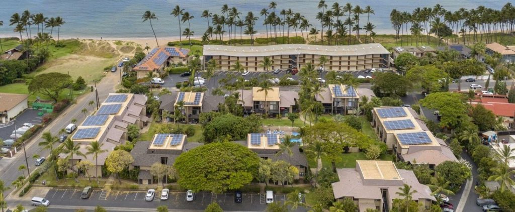 Aerial view of Kihei Garden Estates condo complex in South Kihei, Maui, with solar-paneled rooftops, pool, lush landscaping, and nearby sandy beachfront